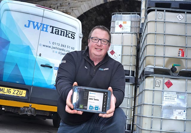 Nick Saunders, Operations Manager at JWH Tanks, holding a BigChange tablet to camera, in front of branded van.
